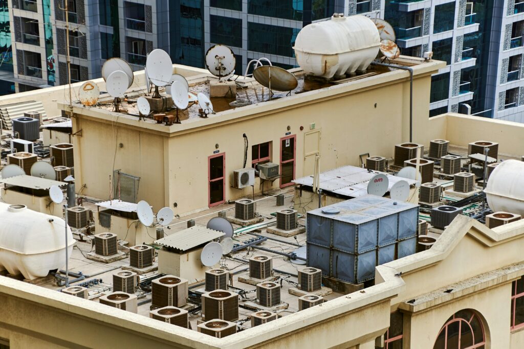 Captured from above, this urban rooftop features satellite dishes, water tanks, and HVAC units, showcasing city infrastructure.