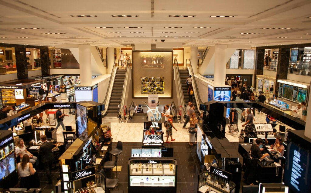 A bustling scene inside a modern shopping mall with escalators and various retail stalls.