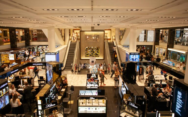A bustling scene inside a modern shopping mall with escalators and various retail stalls.